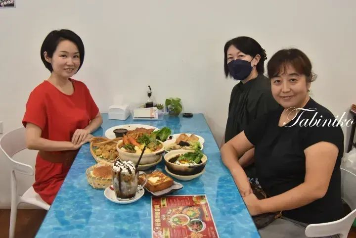 Three women sit at a blue table enjoying a meal of claypot dishes and drinks at a restaurant.