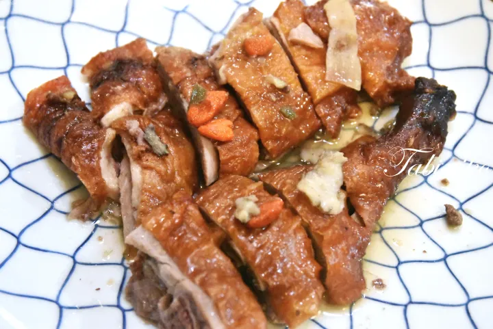 クコの実と生姜を添えた、青い網目模様の皿に盛られた焼き鴨の切り身