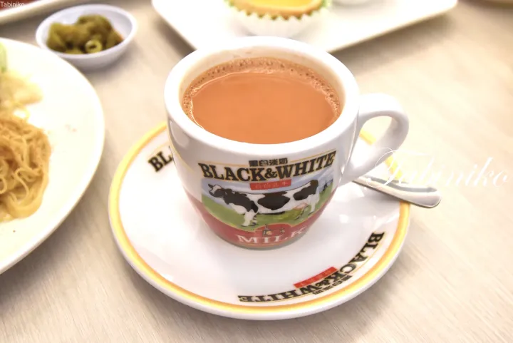 ブラック＆ホワイトのマグとソーサーに入ったミルクコーヒーと、麺料理、小皿の添え物が並んだテーブル。