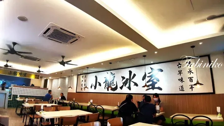 Interior of Xiao Long Cafe featuring large calligraphy signage, wooden tables, and ceiling fans.
