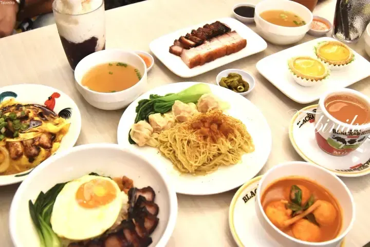 Variety of Malaysian dishes including noodles, roasted meats, egg tarts, and drinks on a table.