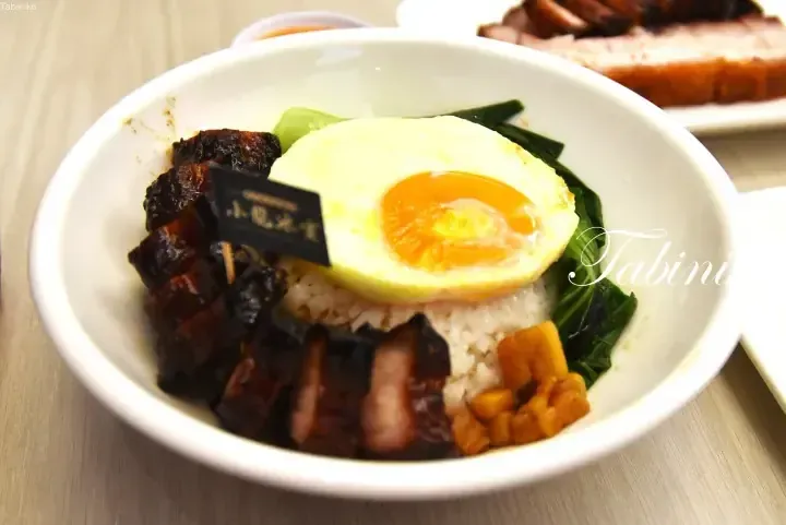 A bowl of rice topped with char siu, a sunny-side-up egg, and vegetables from Xiao Long Ice Room.