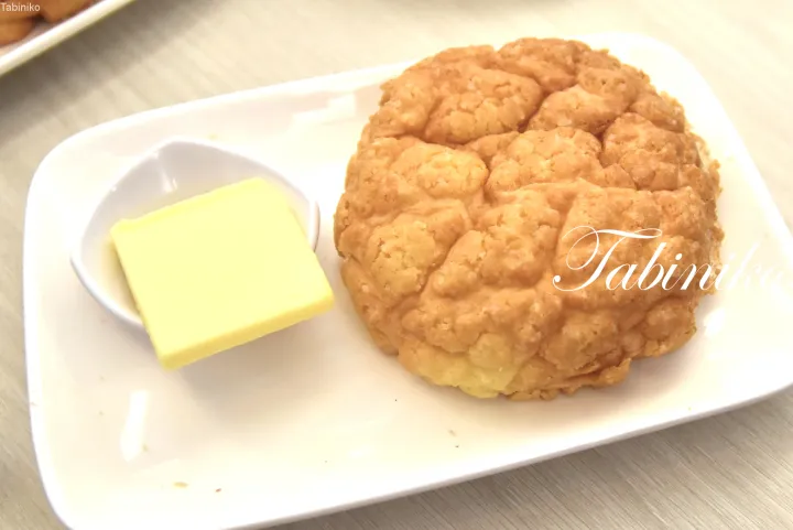 割れ目が入った黄金色のパイナップルパンと、白い皿に添えられたバターの角切り。