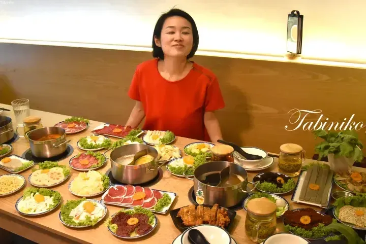Woman in red shirt smiling at a table full of hot pot dishes and ingredients at a restaurant.