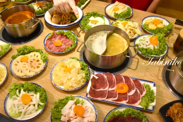 肉、レンコン、野菜などの具材が並び、中央に仕切り鍋が置かれた火鍋のテーブル。