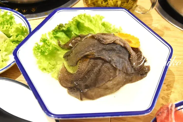 Fresh beef tripe served on a white plate with lettuce, ready for a hot pot meal.