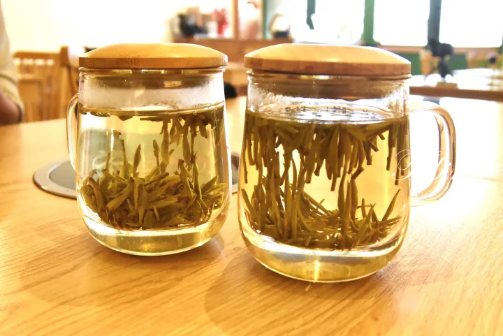 木製の蓋がついたガラスマグカップ2つに注がれた緑茶と茶葉