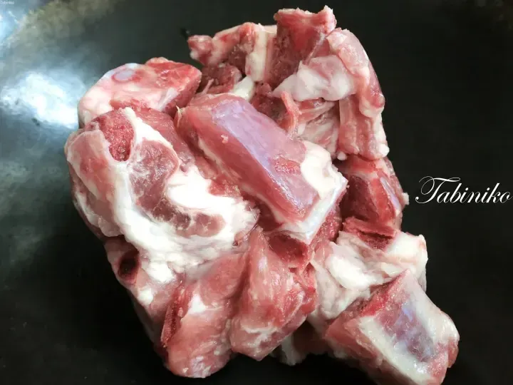Raw pork ribs with bone and fat on a dark surface, watermarked Tabiniko