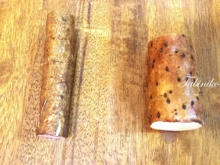 Two pieces of yam on a wooden cutting board, one peeled and one unpeeled with visible root hairs.