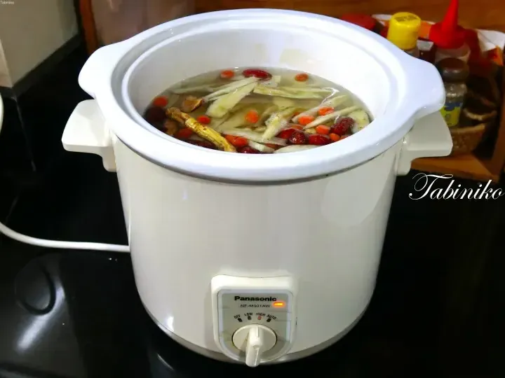 Panasonic slow cooker filled with herbal soup, ginger, and red dates on a kitchen counter.