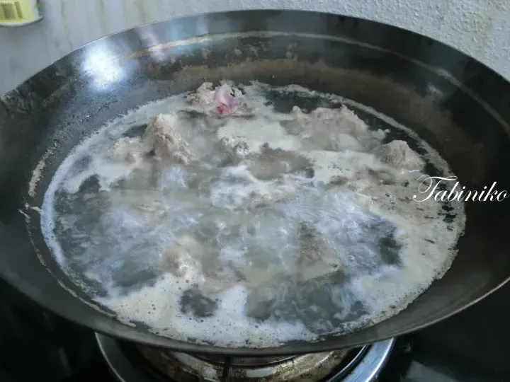 Meat boiling in a wok with frothy water on a stove.