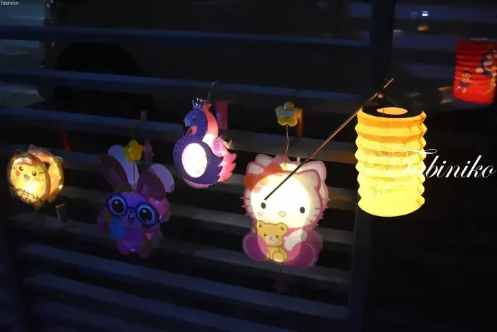 Colorful illuminated character lanterns including Pikachu and Hello Kitty hanging on a railing at night.