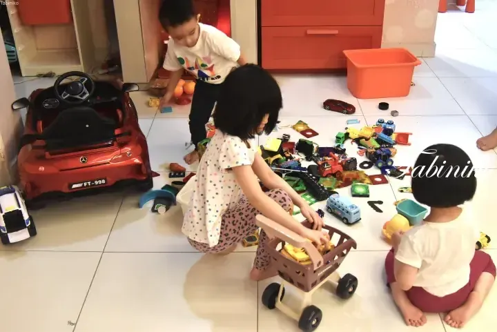 Children playing with toys and a red ride-on car in a modern home living area.