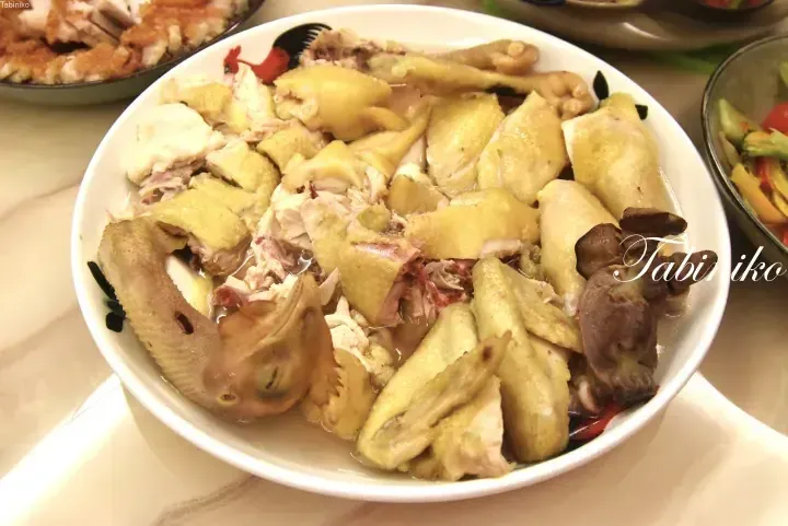 A white bowl filled with chopped steamed chicken pieces, including the head and gizzards, served as a traditional Malaysian dish.