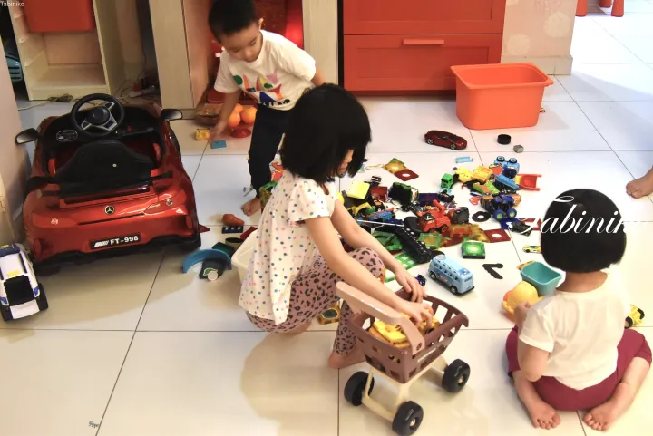 モダンなリビングで赤い乗用玩具と他の遊具で遊ぶ子供たち。