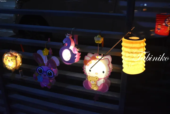夜に手すりに吊るされたピカチュウやハローキティなどのキャラクター提灯。