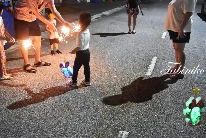 Children playing with sparklers and glowing toys on a street at night.