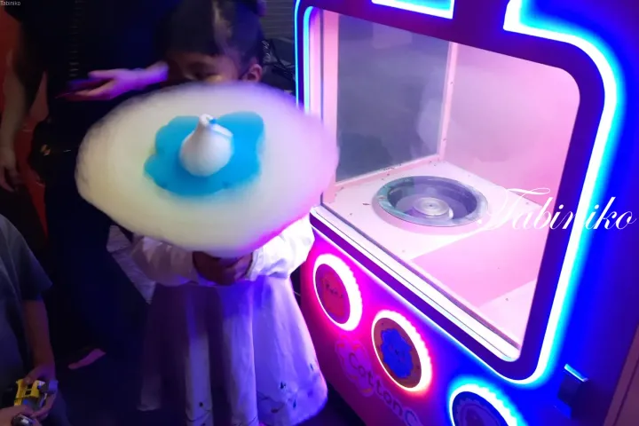 光る綿菓子機の前で大きな青と白の綿菓子を持つ子供。