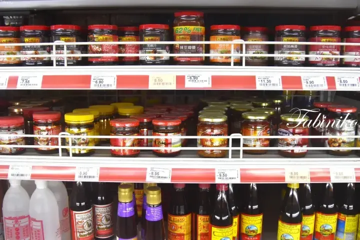 Shelves stocked with Lee Kum Kee sauces and other condiments with price tags at a Malaysian grocery store.
