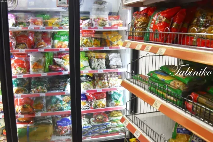 Frozen food aisle in a Malaysian supermarket with glass-door freezers stocked with fish balls and steamboat selection, next to dry goods shelves.