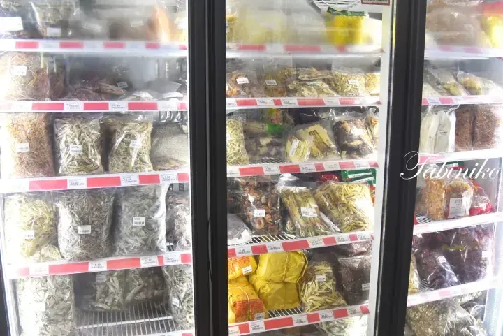 Refrigerated shelves stocked with various packaged dried seafood, herbs, and ingredients in a Malaysian grocery store.