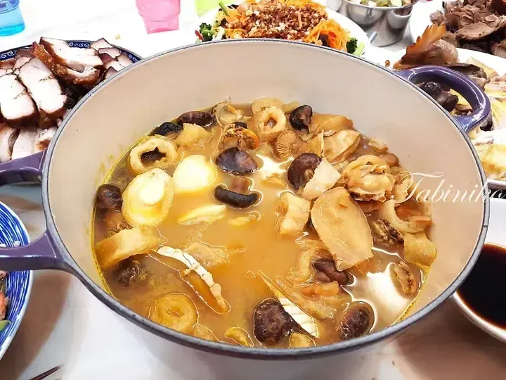 A pot of rich abalone and mushroom hot pot surrounded by platters of roasted pork and other dishes.