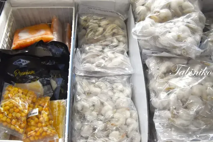 Open freezer containing bags of IQF Vannamei Shrimp, frozen corn, and Kanika Premium seafood products.
