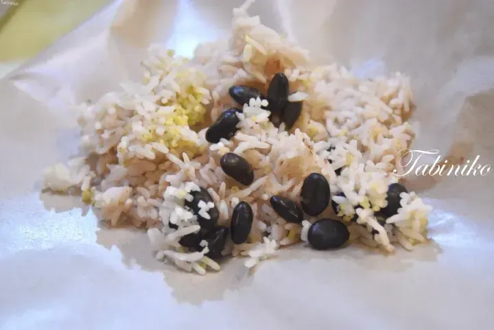 A serving of rice mixed with black beans and yellow grains on a white paper wrapper.