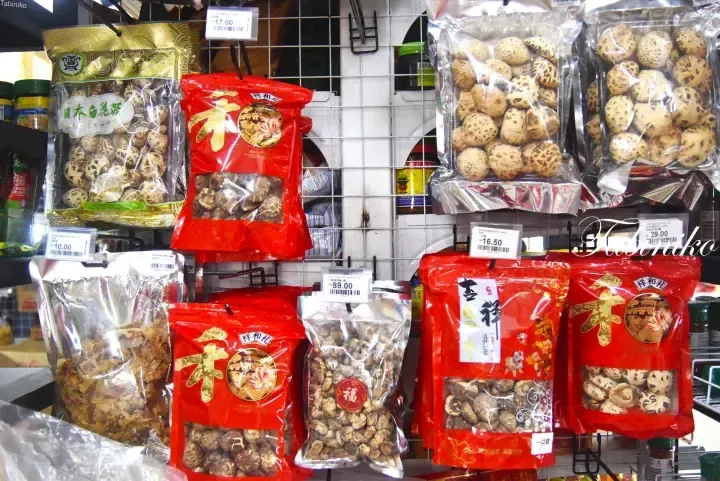 Assorted dried mushrooms in red and gold packaging displayed on a wire rack at a Malaysian grocery store.