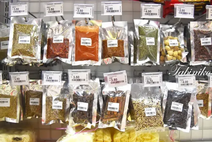 Various spices in sealed packets hanging on a display rack with price tags in Malaysian Ringgit at a Malaysian market.
