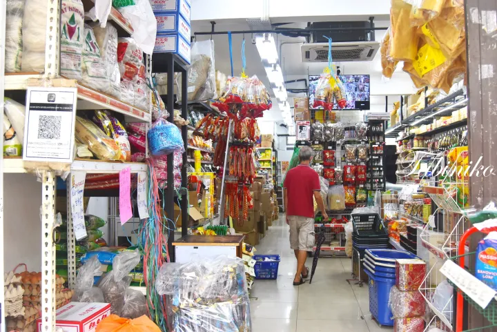 スナックや包装食品で満たされた狭い通路を歩く男性が写るマレーシアの食料品店の店内。