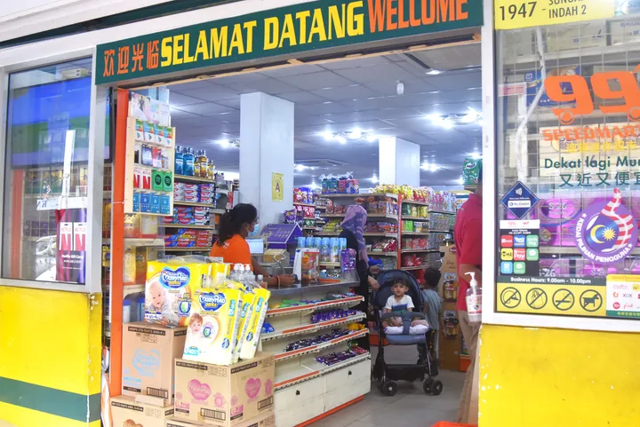 「Selamat Datang」の看板が目立つ99 Speedmartの入り口と店内の棚、買い物客。