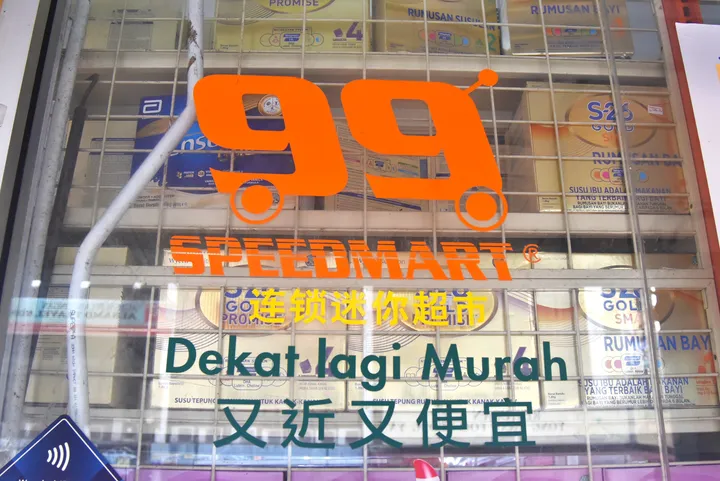 オレンジのスクーターロゴと「Dekat lagi Murah」「又近又便宜」の多言語看板が目立つスピードマート店舗の外観。