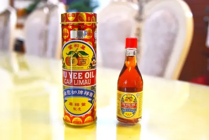 A tin and glass bottle of Yu Yee Oil Cap Limau, a traditional Malaysian herbal remedy, displayed on a table.