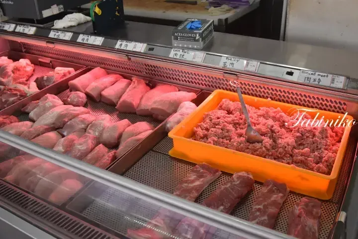 Fresh pork cuts and minced meat displayed in a refrigerated butcher counter with bilingual labels.