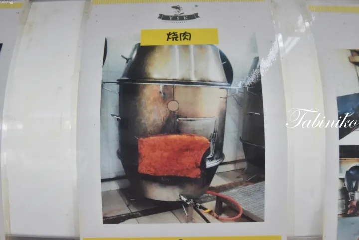 赤いレンガの開口部を持つ大型金属製ロースターと、黄色いラベルに「焼肉」と書かれた写真。