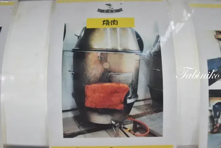 A large metal roasting oven with a red brick opening and a yellow label reading “Shao Rou” (roasted meat).