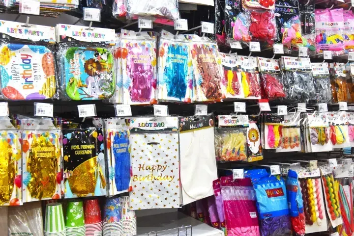 Shelves stocked with colorful birthday party supplies including foil fringe curtains, balloons, and loot bags.