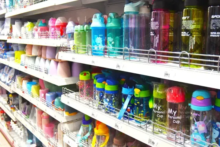 Colorful water bottles and cups arranged on white shelves in a retail store.