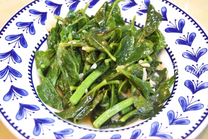 盛裝在帶有藍色花卉圖案白盤中的蒜蓉炒菠菜。