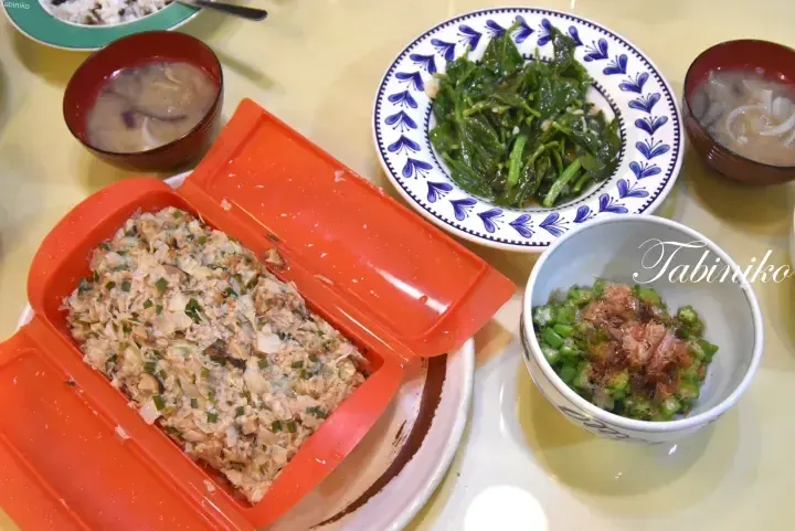 A bento box with tuna salad, okra, spinach, and miso soup on a table.