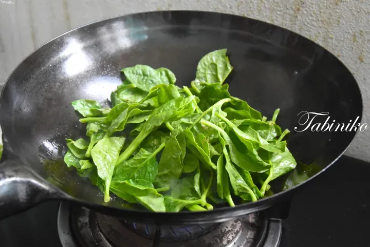 在瓦斯爐上的黑色炒鍋中翻炒的新鮮綠葉菠菜。
