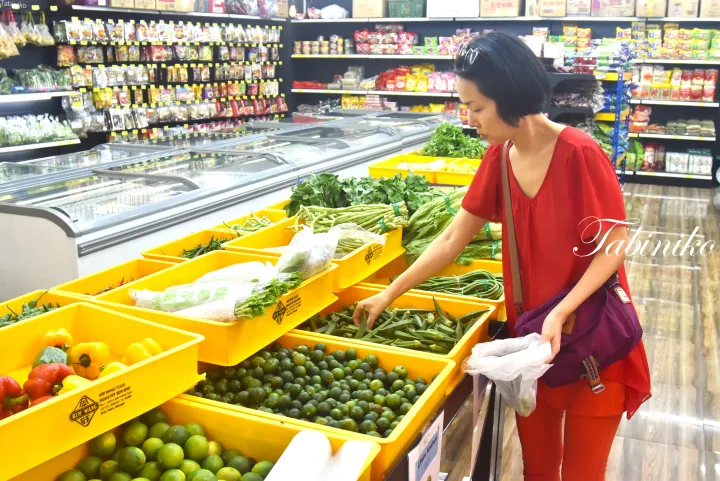 赤い服を着た女性がマレーシアのスーパーマーケットで黄色い箱から新鮮な野菜を選んでいる。