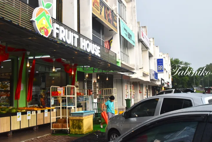 新鮮な果物の陳列とオレンジ色の袋を持った人がいるFruit Houseの店舗外観。