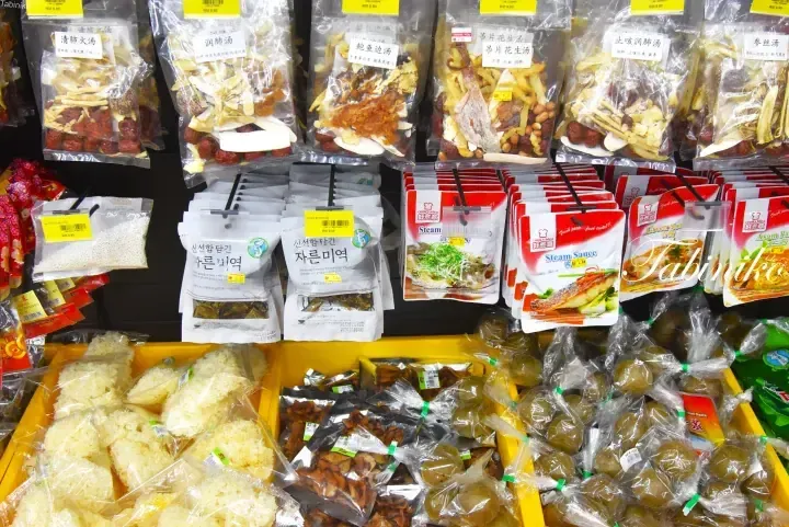 Shelves stocked with various packaged dried ingredients, herbal soups, and sauces in a Malaysian grocery store.