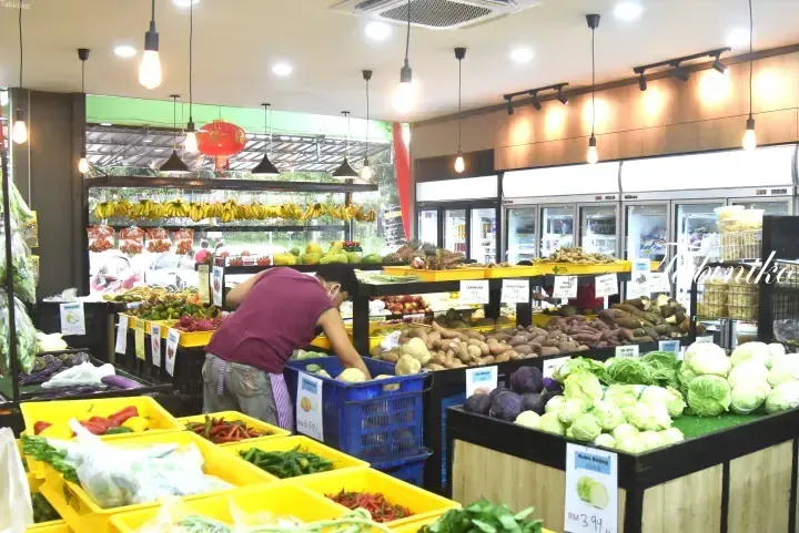 Staff arranging fresh produce in a well-lit supermarket with hanging bananas and refrigerated sections.