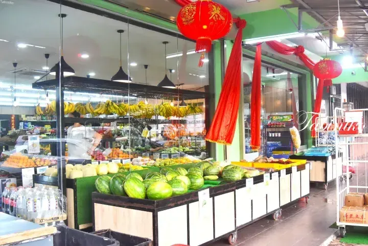 Fresh fruit display at a Malaysian supermarket featuring watermelons, bananas, and red lanterns.