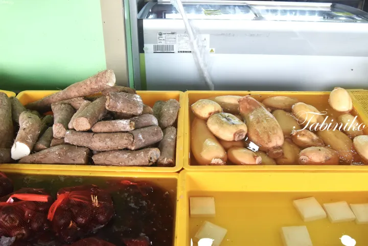 タロイモ、蓮根、赤玉ねぎなど、マレーシアの食材が黄色いトレイに並べられた市場の風景。