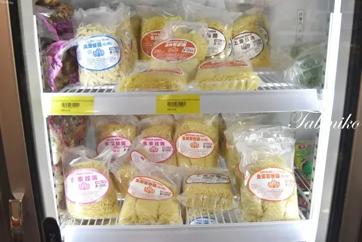 Refrigerated display shelves stocked with various packaged fresh noodles, including Hakka Ramen and Wantan Mee.