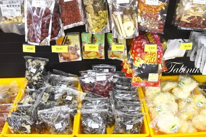 Shelves stocked with various dried herbs, soups, and ingredients like red dates and mushrooms in a Malaysian grocery store.